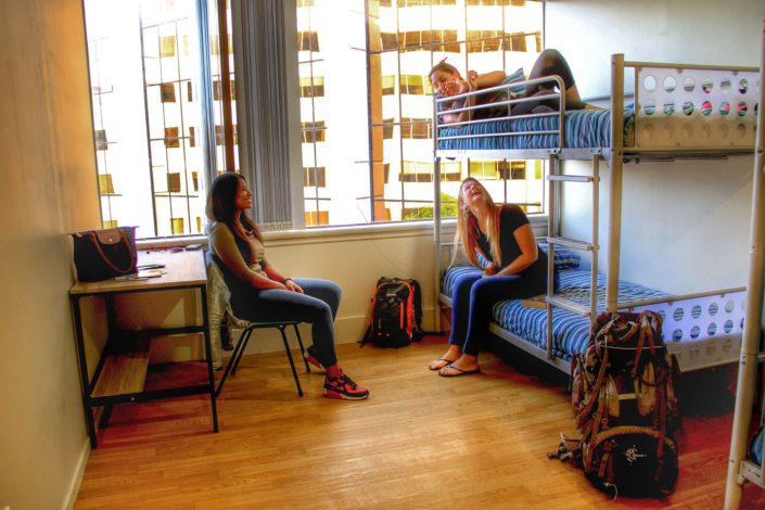 Image of a 4 bed dorm showing 3 people sitting and lying on bunk beds
