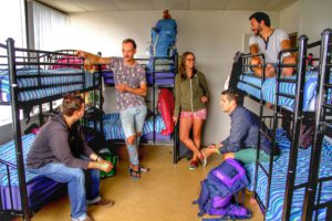 Image of an 8 bed dorm in a backpackers showing some guests standing next to bunk beds