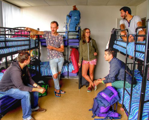 Image of an 8 bed dorm in a backpackers showing some guests standing next to bunk beds