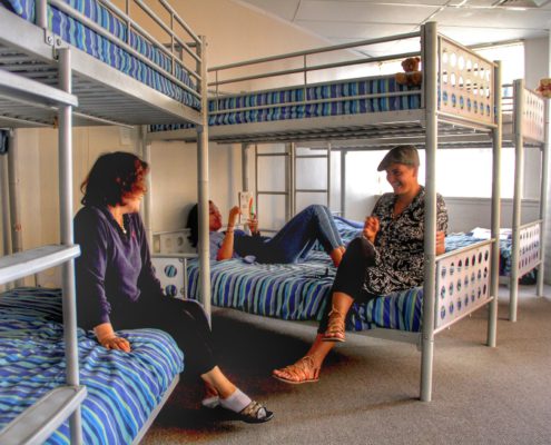 Image of a 6 bed dorm in a backpackers showing guests lying and sitting on bunk beds