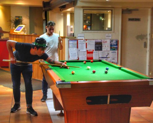 Image of 2 people playing pool in the lobby of the backpacker