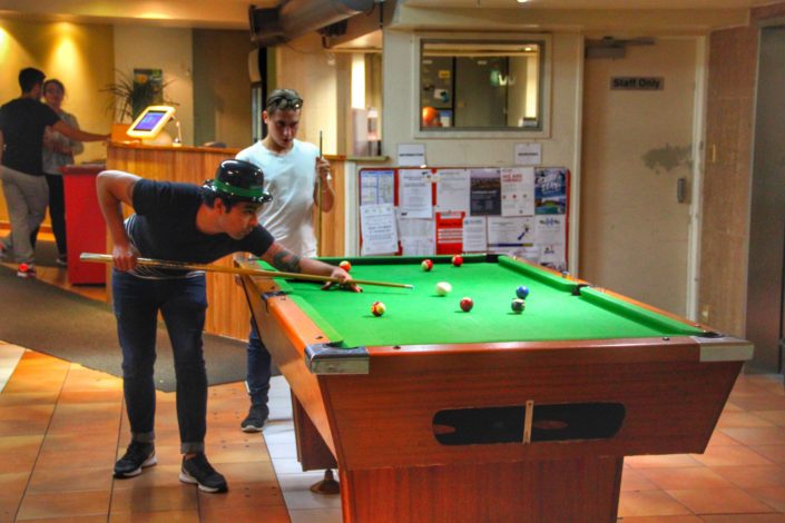 Image of 2 people playing pool in the lobby of the backpacker